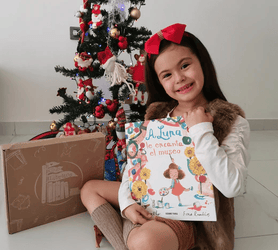 Niña feliz por las fiestas familiares y la decoración navideña, con su libro en mano de Club Libritos, sabiendo la importancia de leer cuentos navideños a los niños, así como realizar actividades navideñas para niños y padres