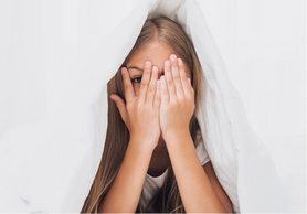 Niña con miedo debajo de las sabanas, teniendo que aprender a como afrontar el miedo escolar y la ansiedad social infantil a través de ejercicios, métodos y estrategias para enfrentar sus miedos 